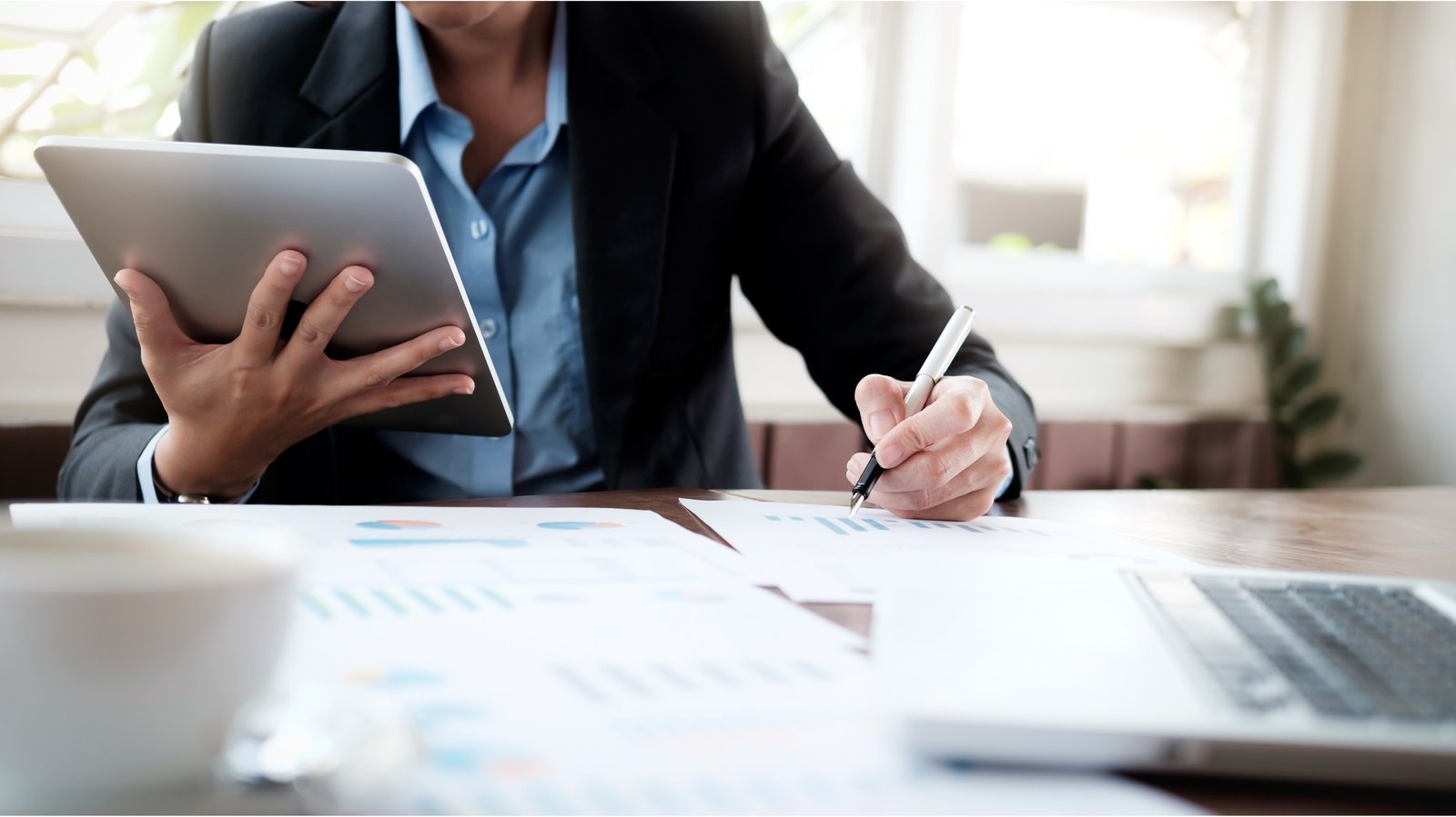 uomo alla scrivania che scrive e ha in mano un tablet
